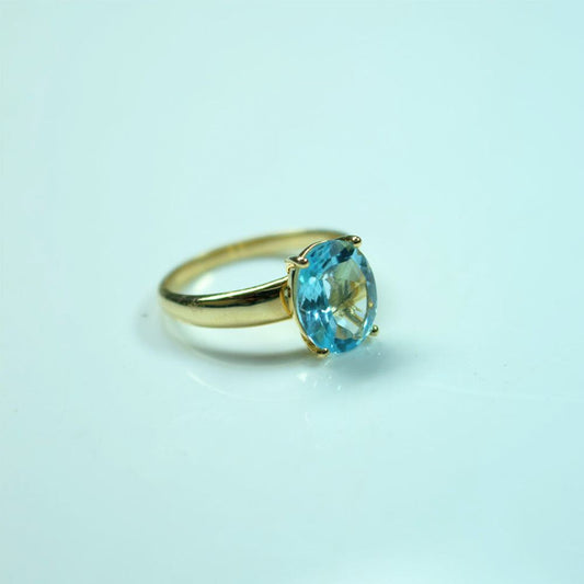Gold ring with a blue gemstone on a light blue background