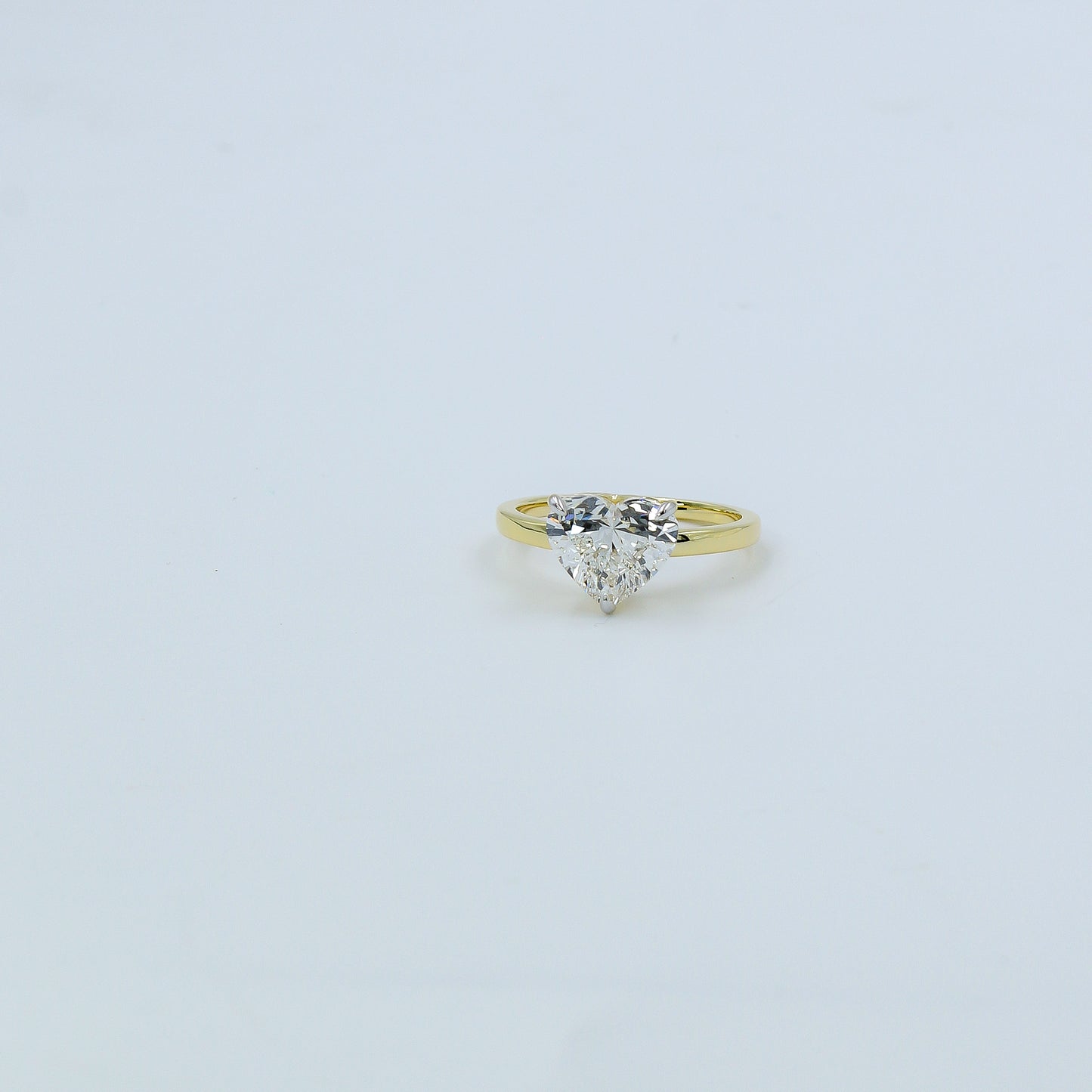 Gold ring with a heart-shaped diamond on a light gray background