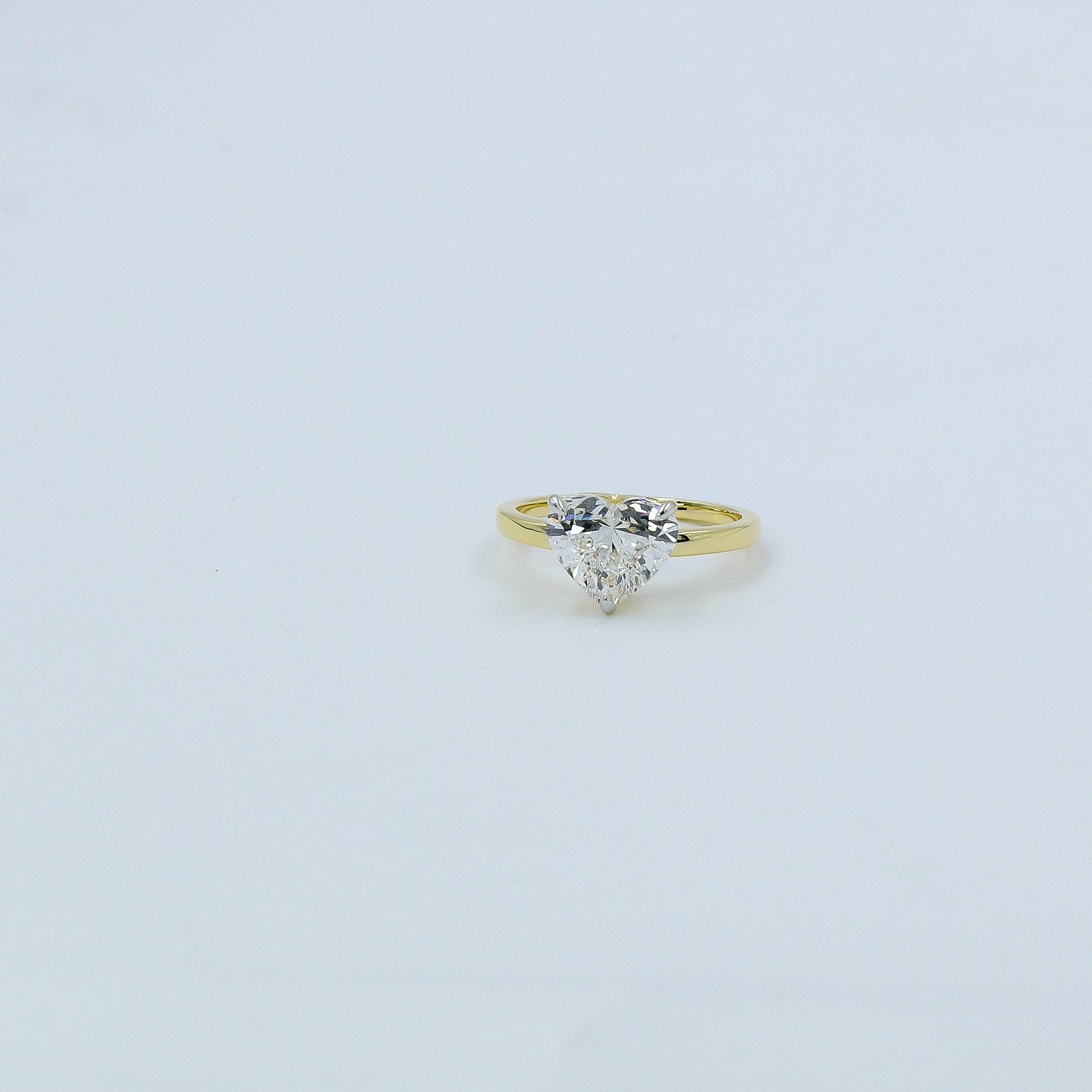Gold ring with a heart-shaped diamond on a light gray background