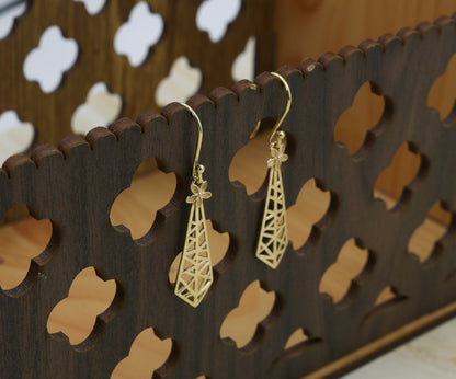 Gold earrings on a wooden stand with cut-out patterns