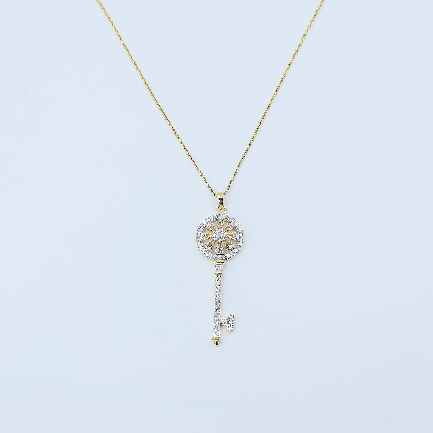 Gold necklace with a key-shaped pendant on a light blue background