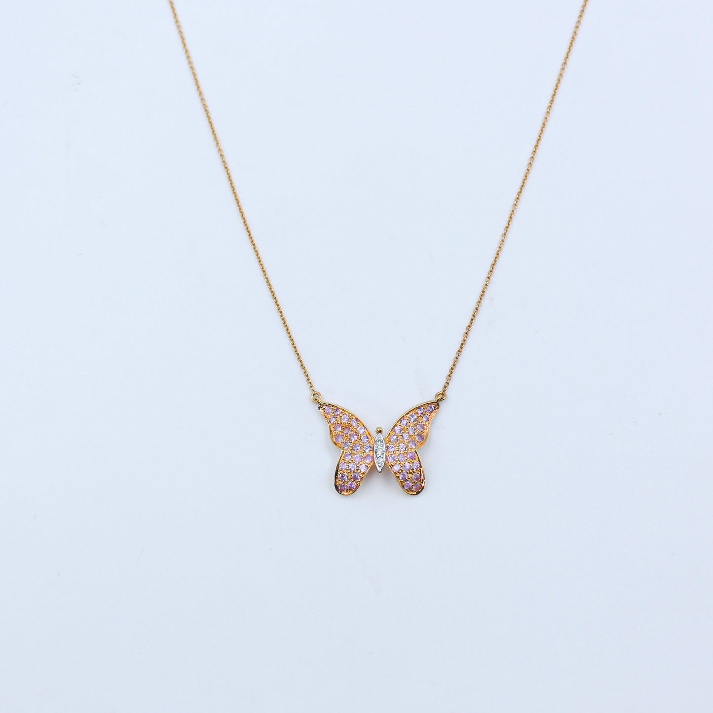 Butterfly-shaped necklace with pink gemstones on a light blue background