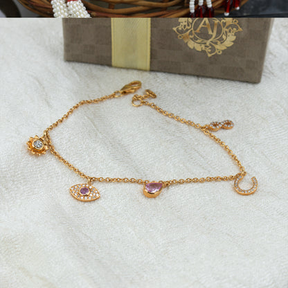 Gold bracelet with charms on a white surface, with a box in the background