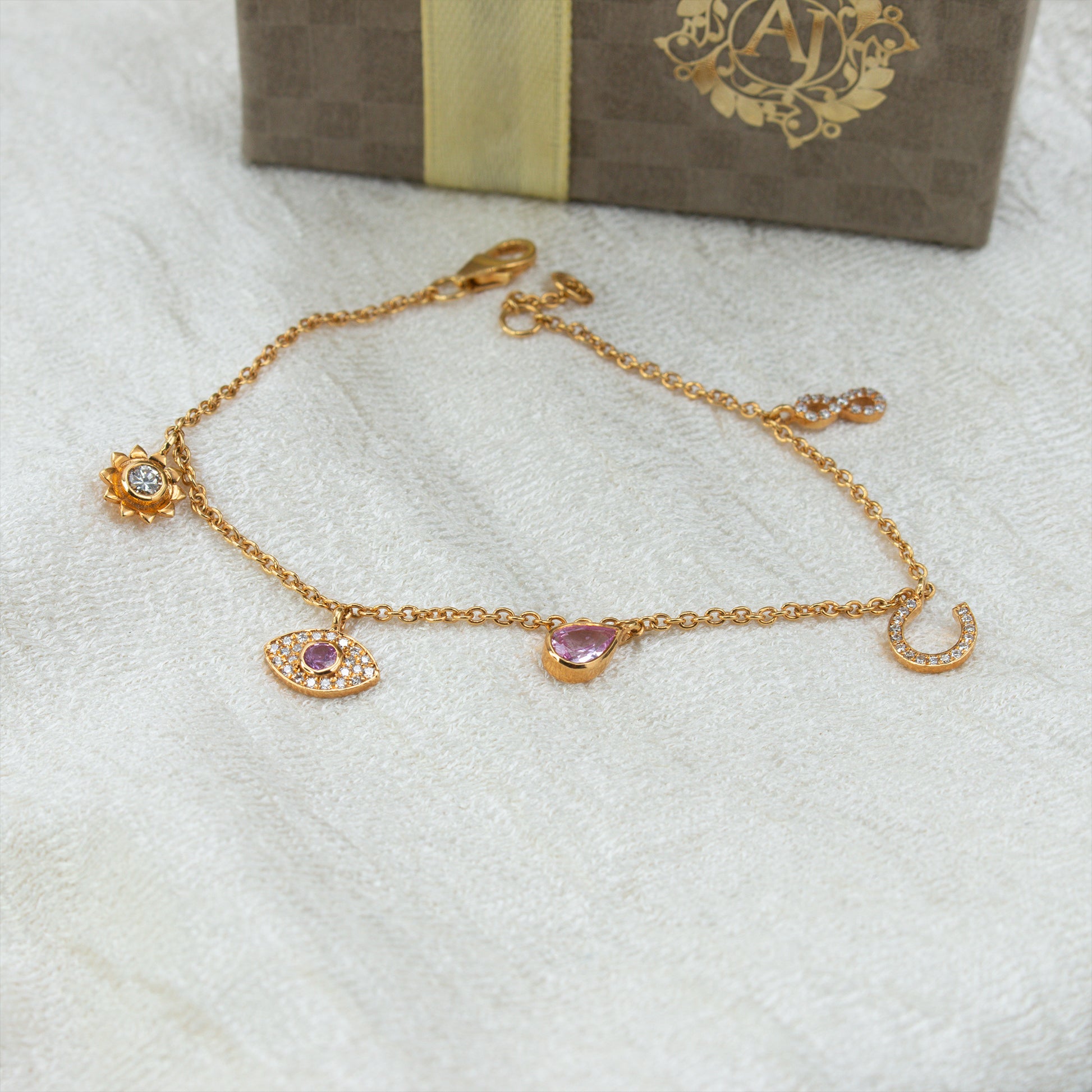 Gold bracelet with charms on a white surface with a branded box in the background