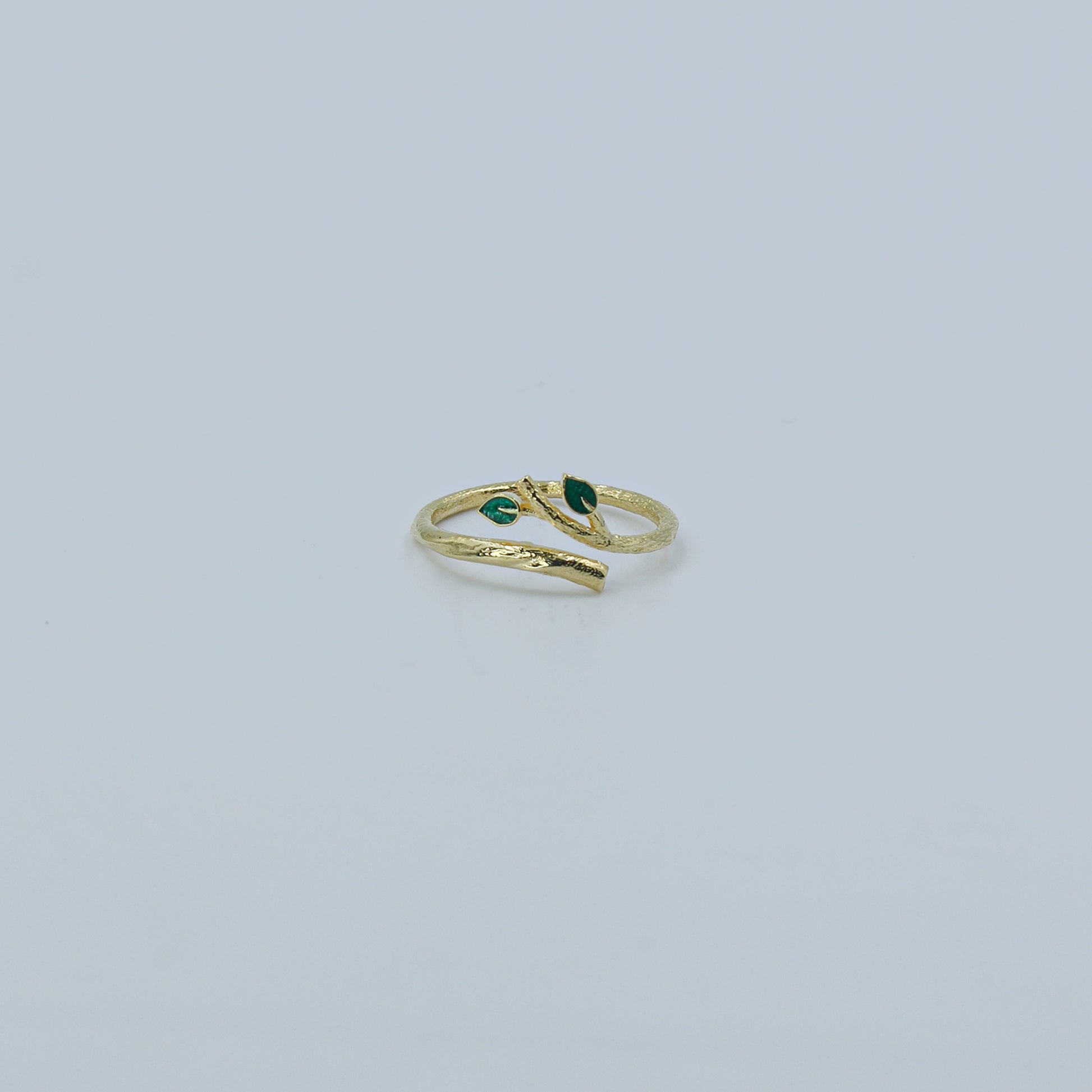 Gold ring with green gemstones on a light gray background