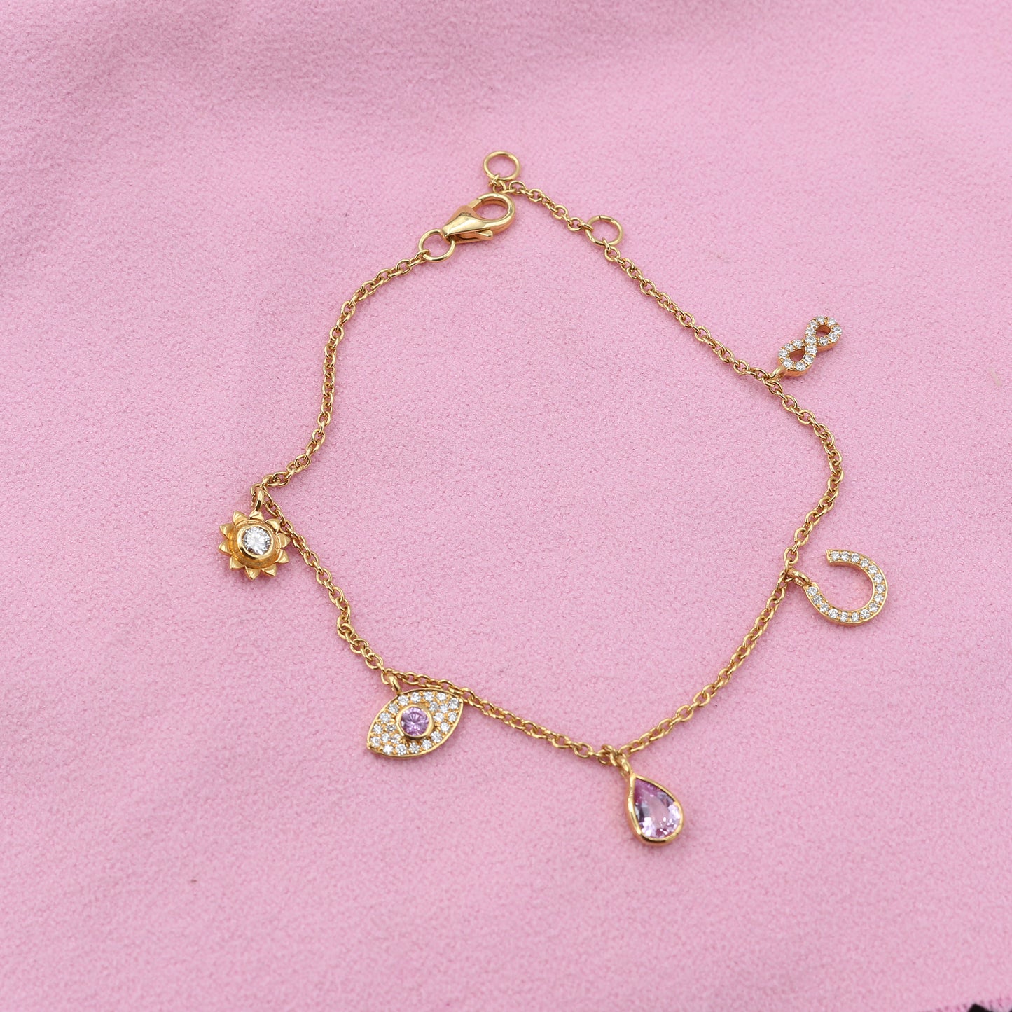Gold bracelet with various charms on a pink background