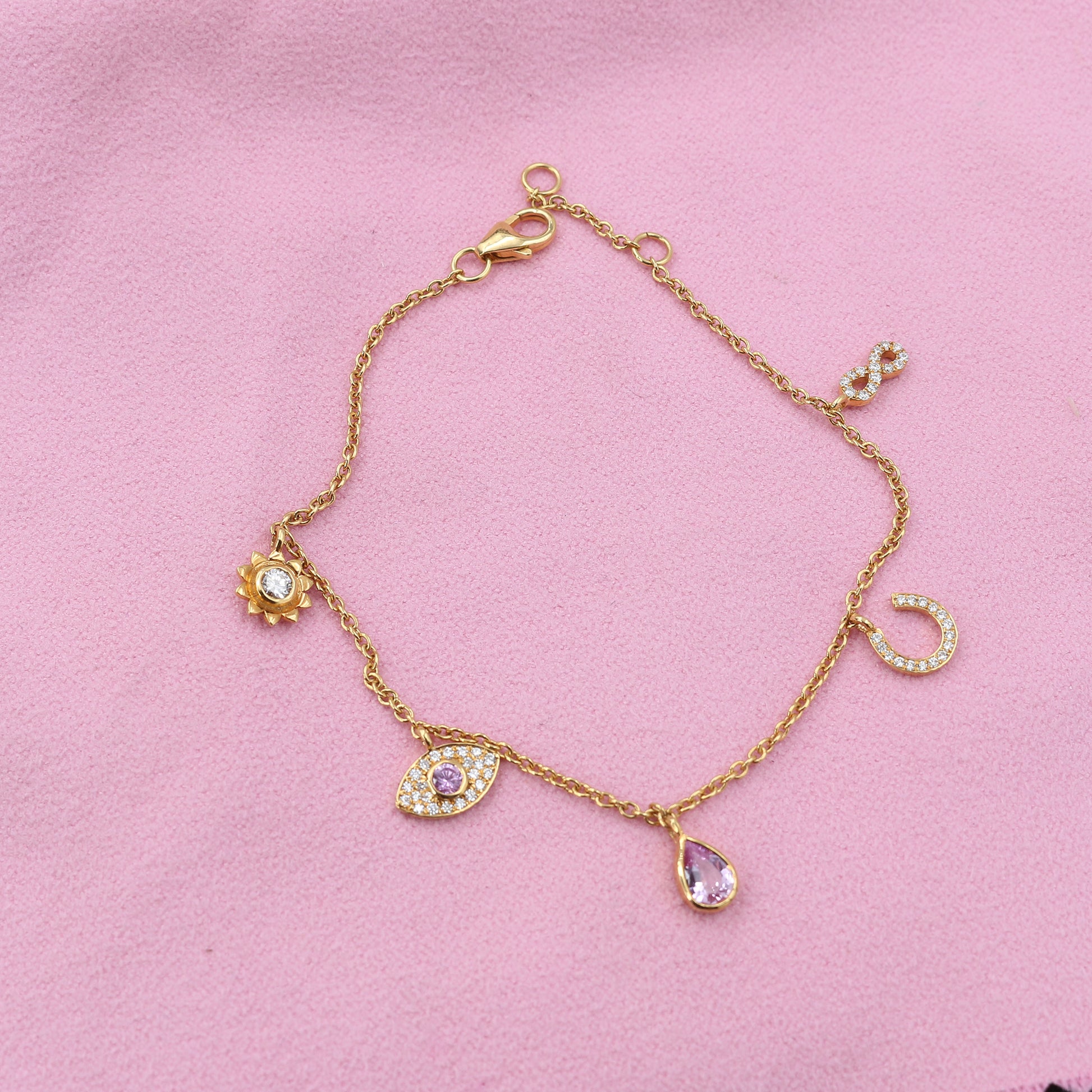 Gold bracelet with various charms on a pink background