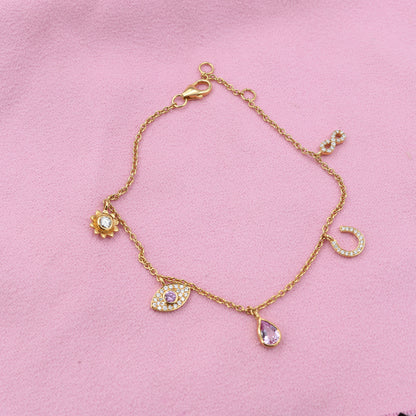 Gold bracelet with various charms on a pink background